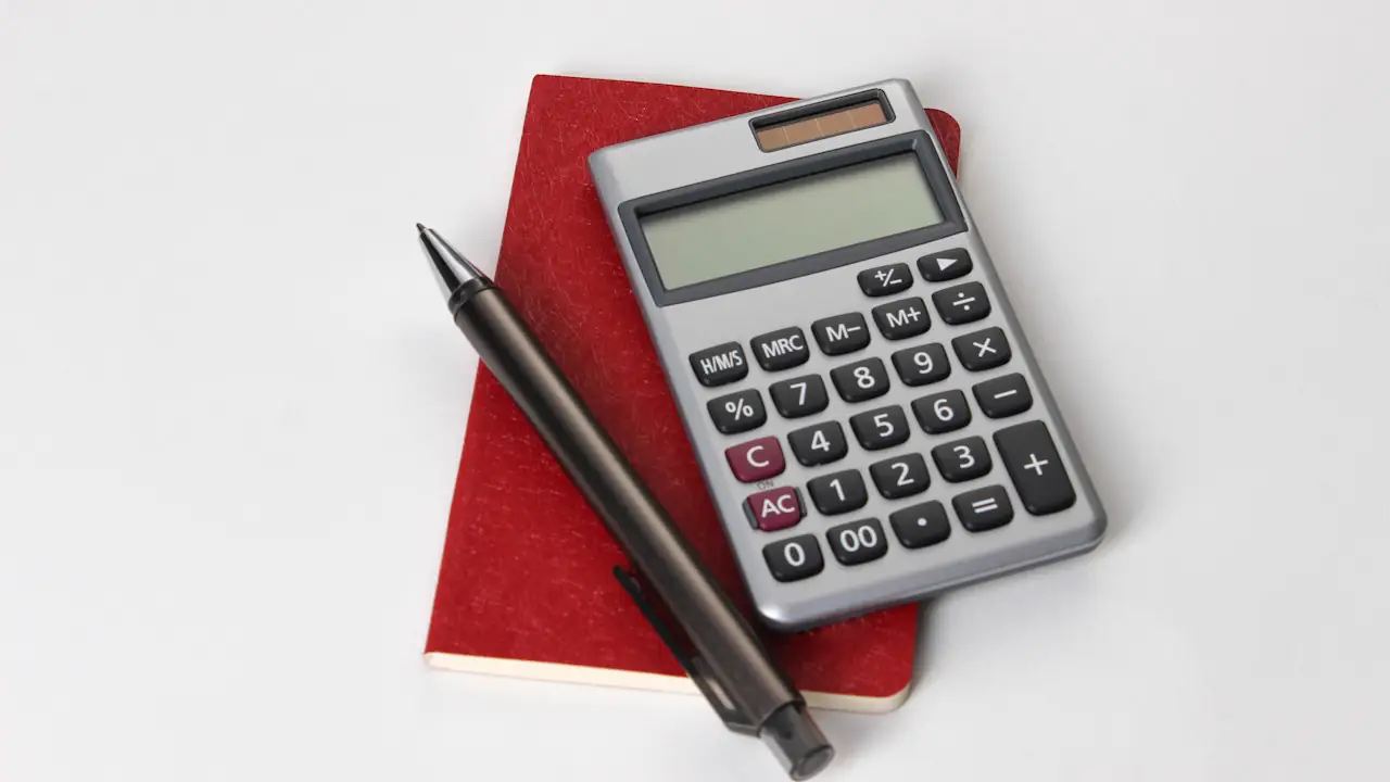 A calculator and a pen resting on a red notebook