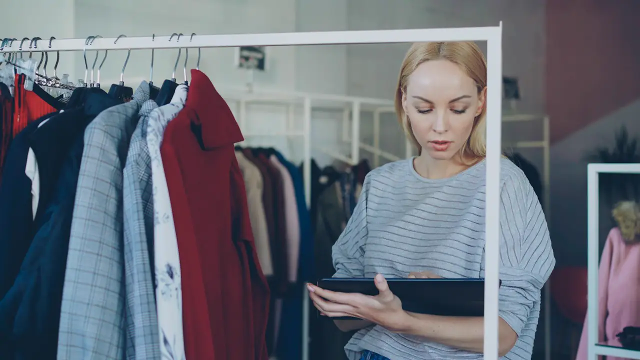 A boutique owner checking stock on a tablet beside a clothing rack