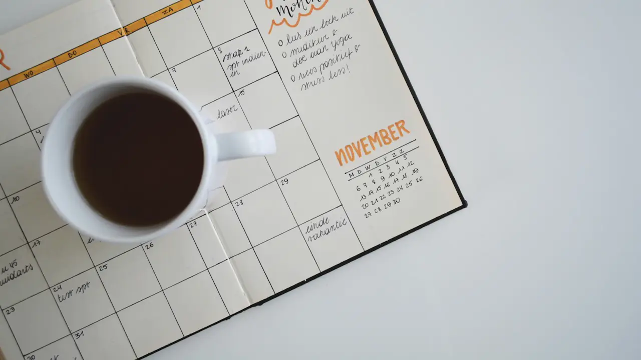 A cup of coffee resting on an open monthly planner with handwritten notes