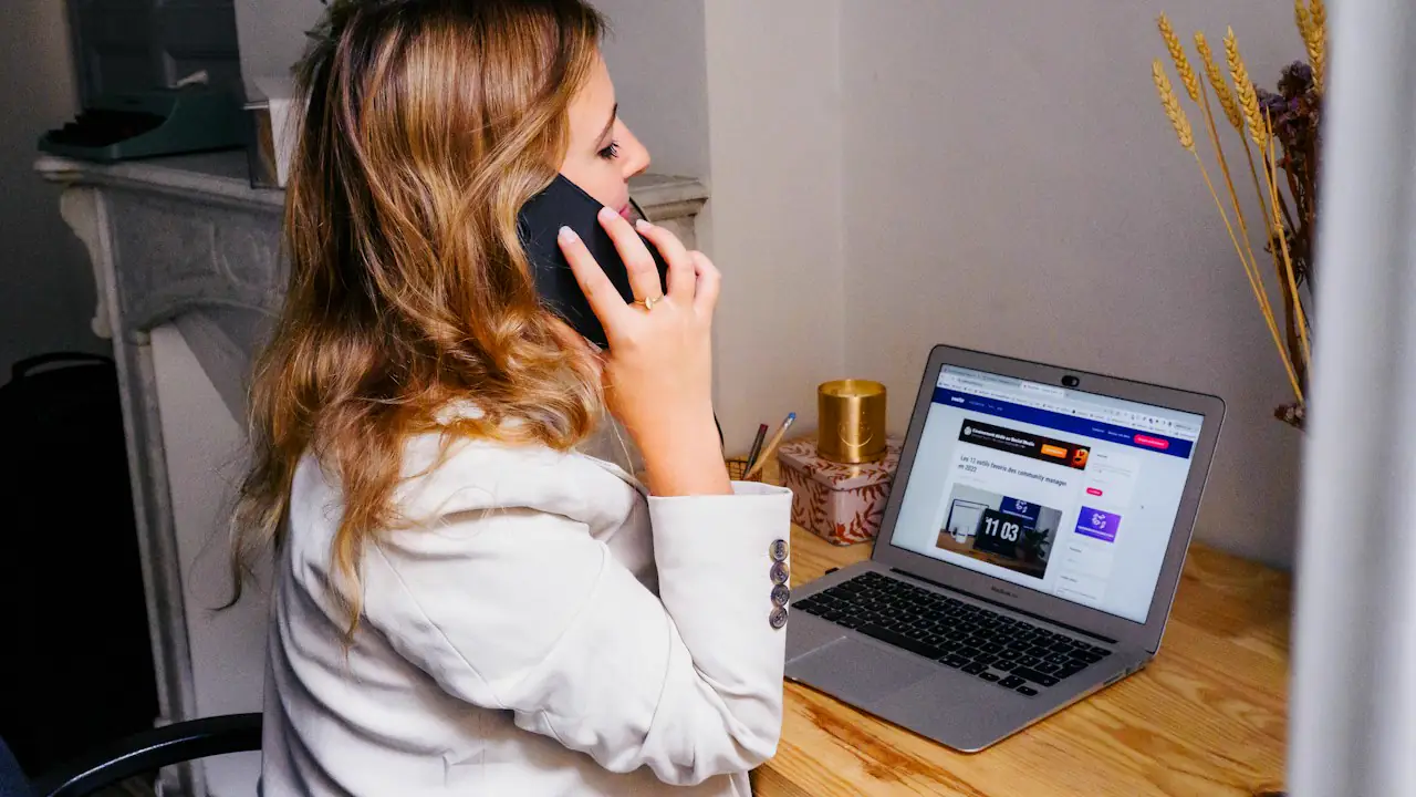 A woman on a phone call at her desk with an open laptop beside her