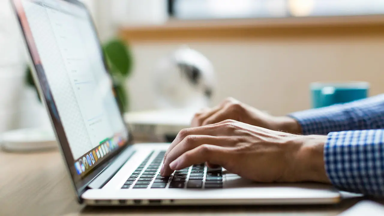 Hands typing on a laptop at a desk by a window
