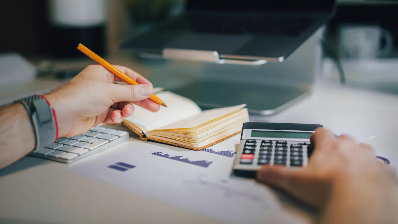 Hands working through figures with a calculator, a pencil and a notebook