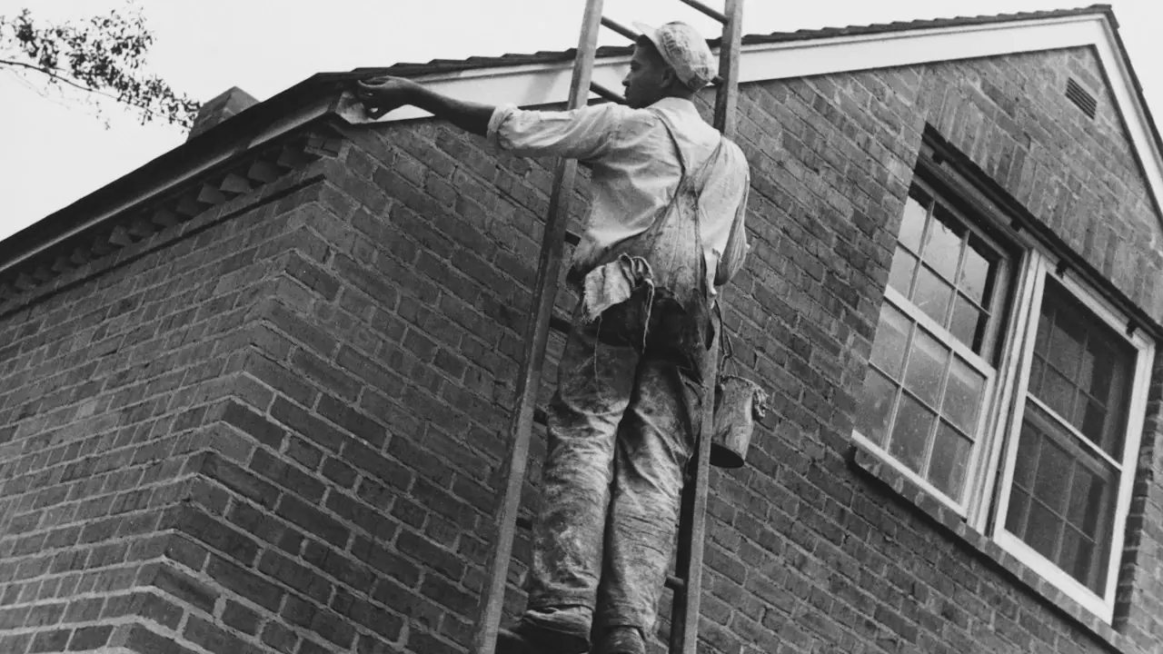 A painter on a ladder working on the trim of a brick house