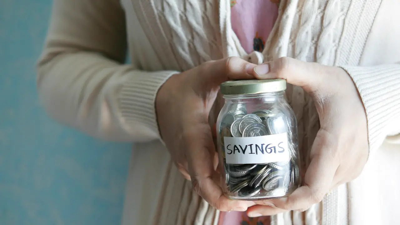 Hands holding a glass jar of coins labelled savings