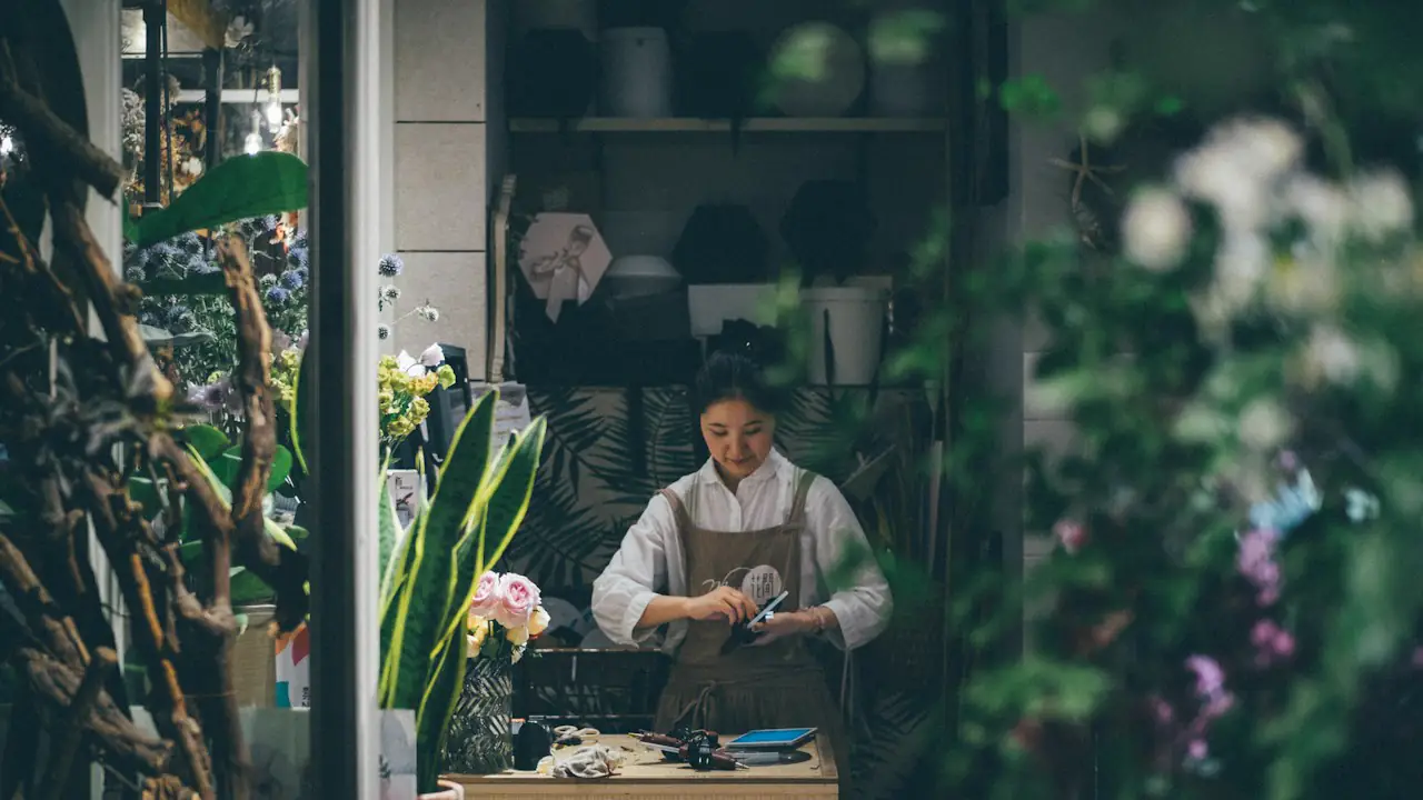 A florist working at the counter of a shop filled with plants