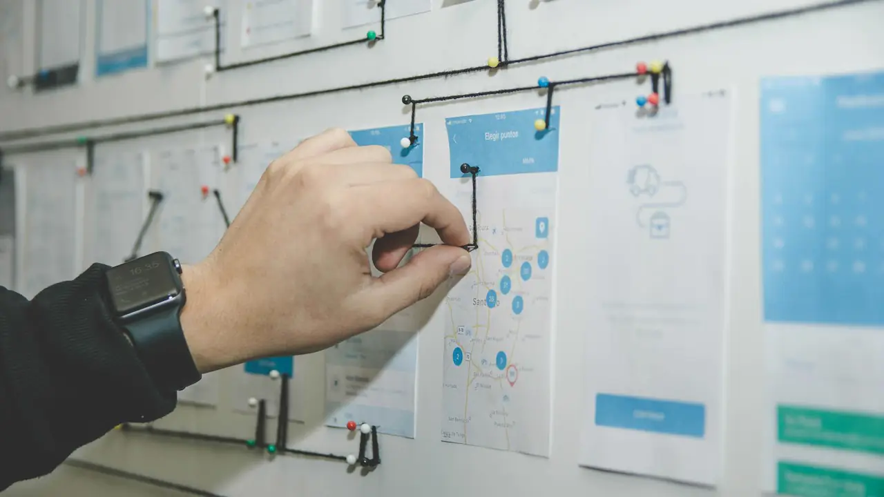 A hand pinning cards and string to a project planning board on a wall