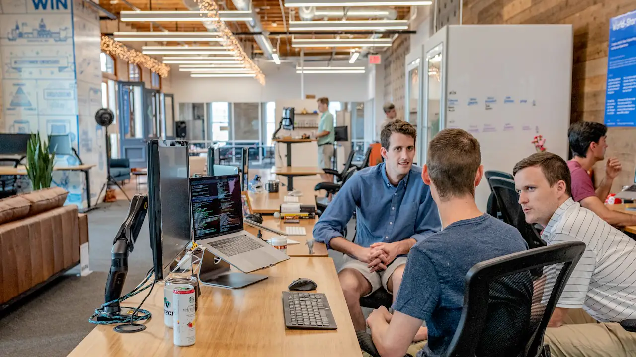 A small team talking around desks with laptops in a bright open plan office