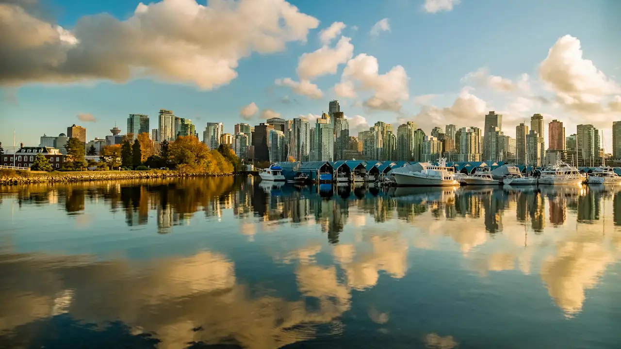 Downtown Vancouver towers reflected in calm water beside a marina