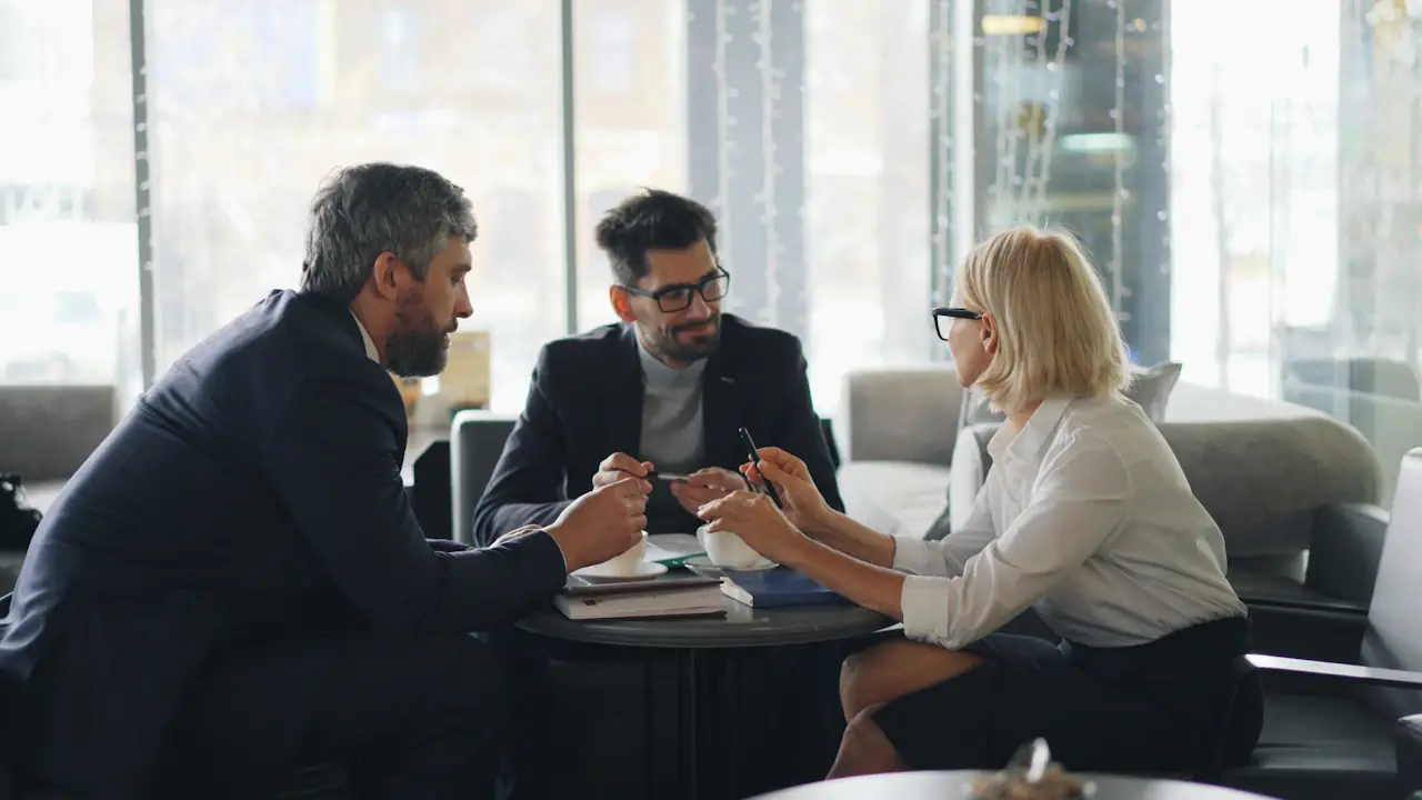 Three colleagues in conversation around a table in a bright lounge