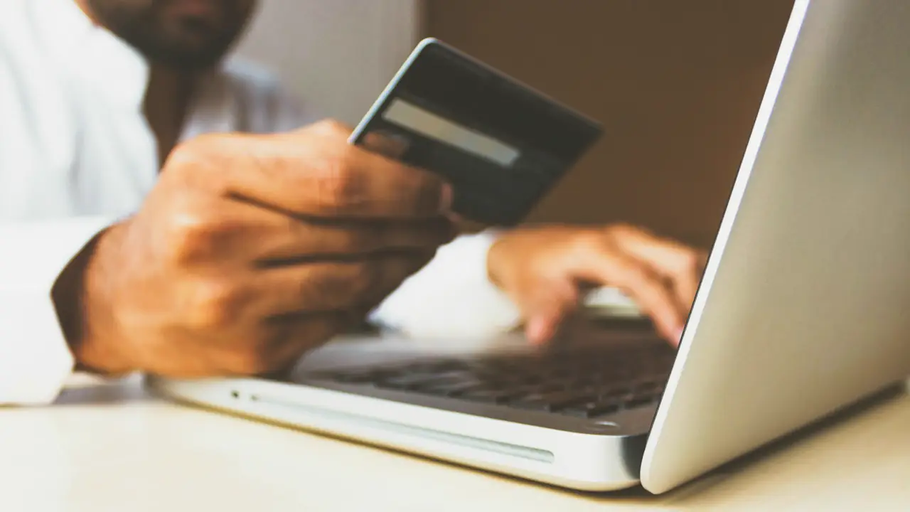Hands holding a bank card while typing on a laptop