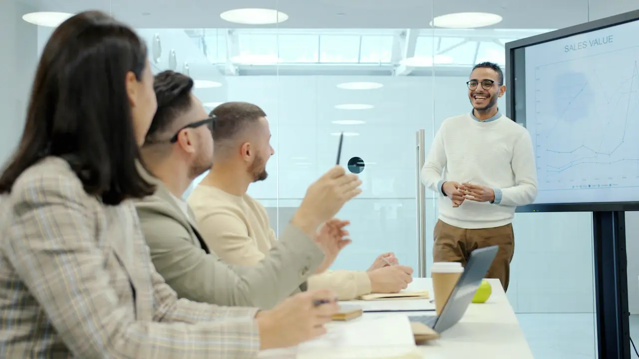 A smiling presenter talking a small team through figures in a bright meeting room