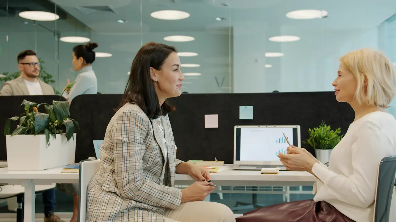 Two women discussing a report across a desk in a bright open office