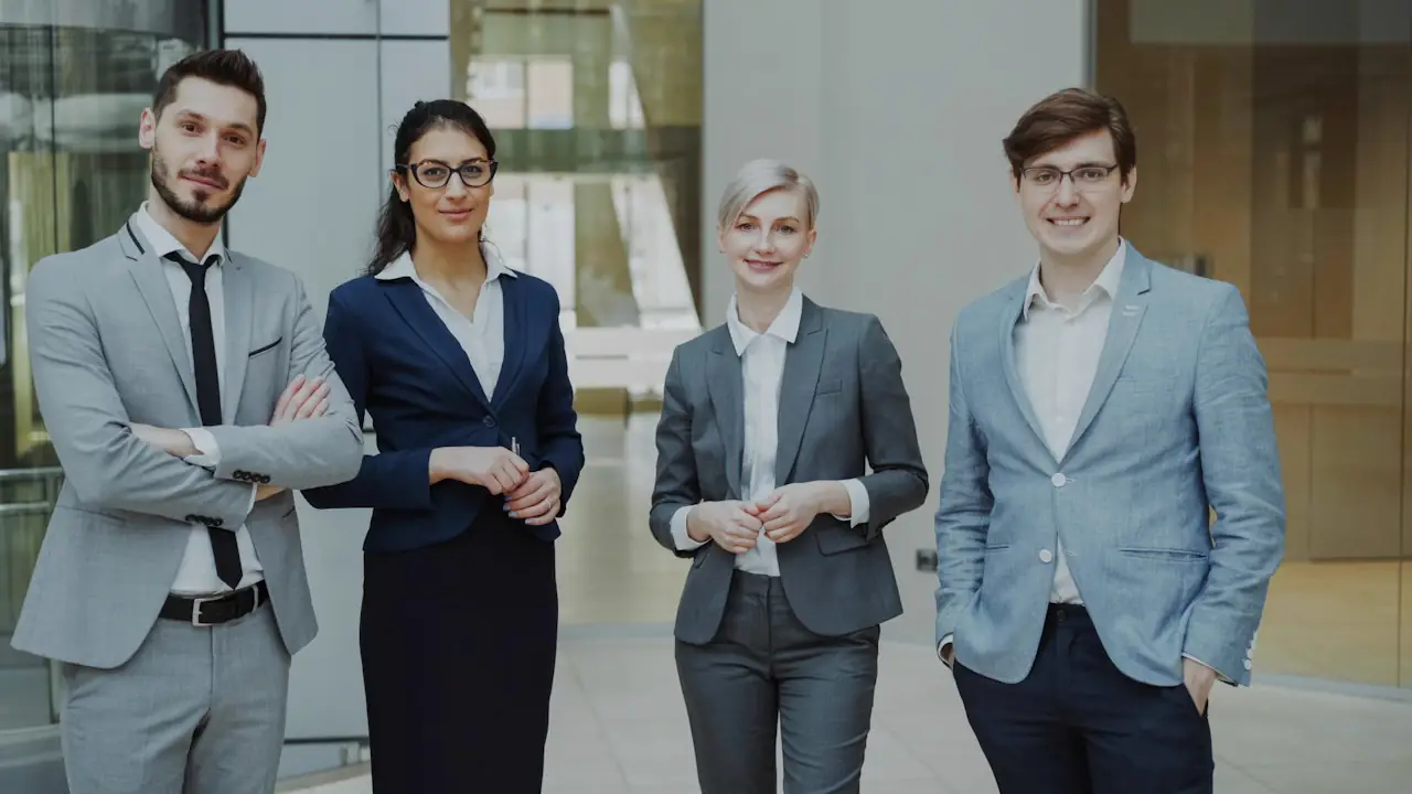 Four smiling professionals in business suits standing together in an office lobby