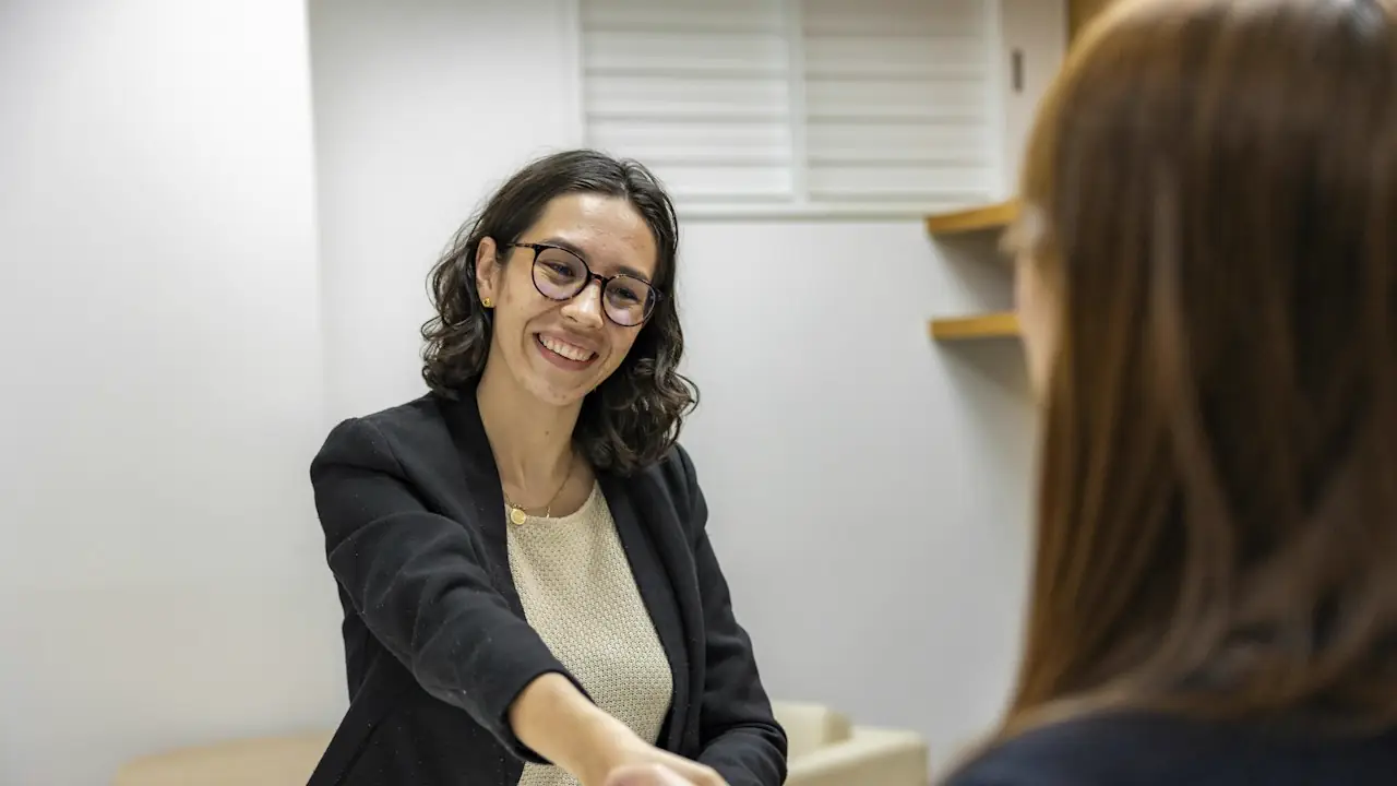A smiling woman in glasses shaking hands across a table