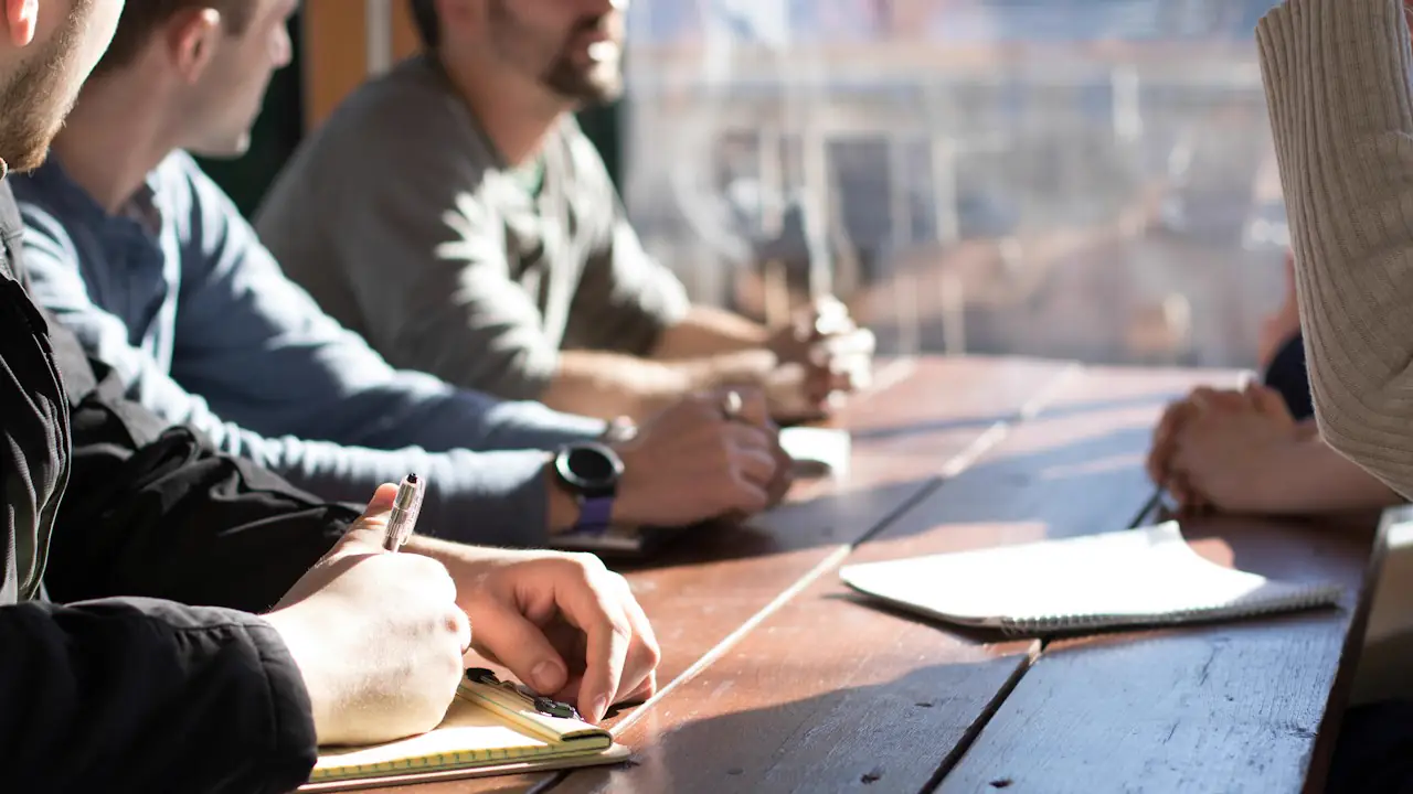 People taking notes around a wooden meeting table