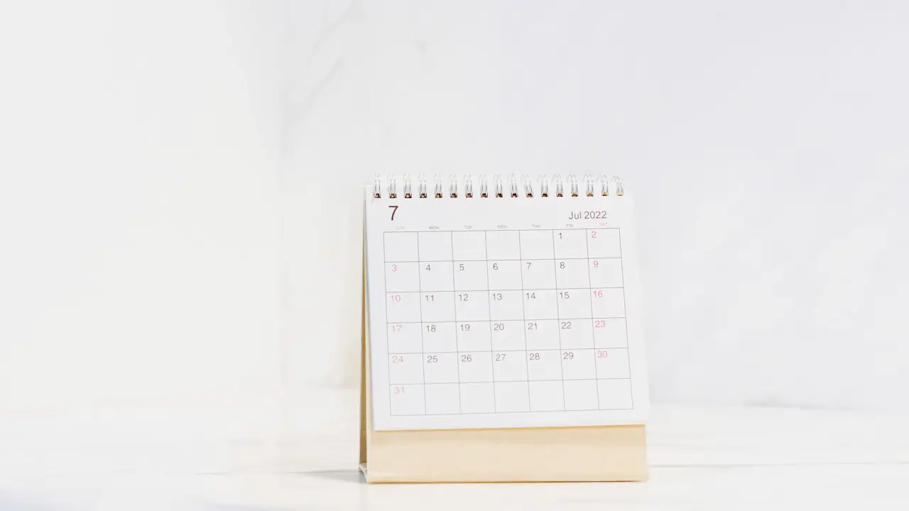 A small white desk calendar standing on a bright white table