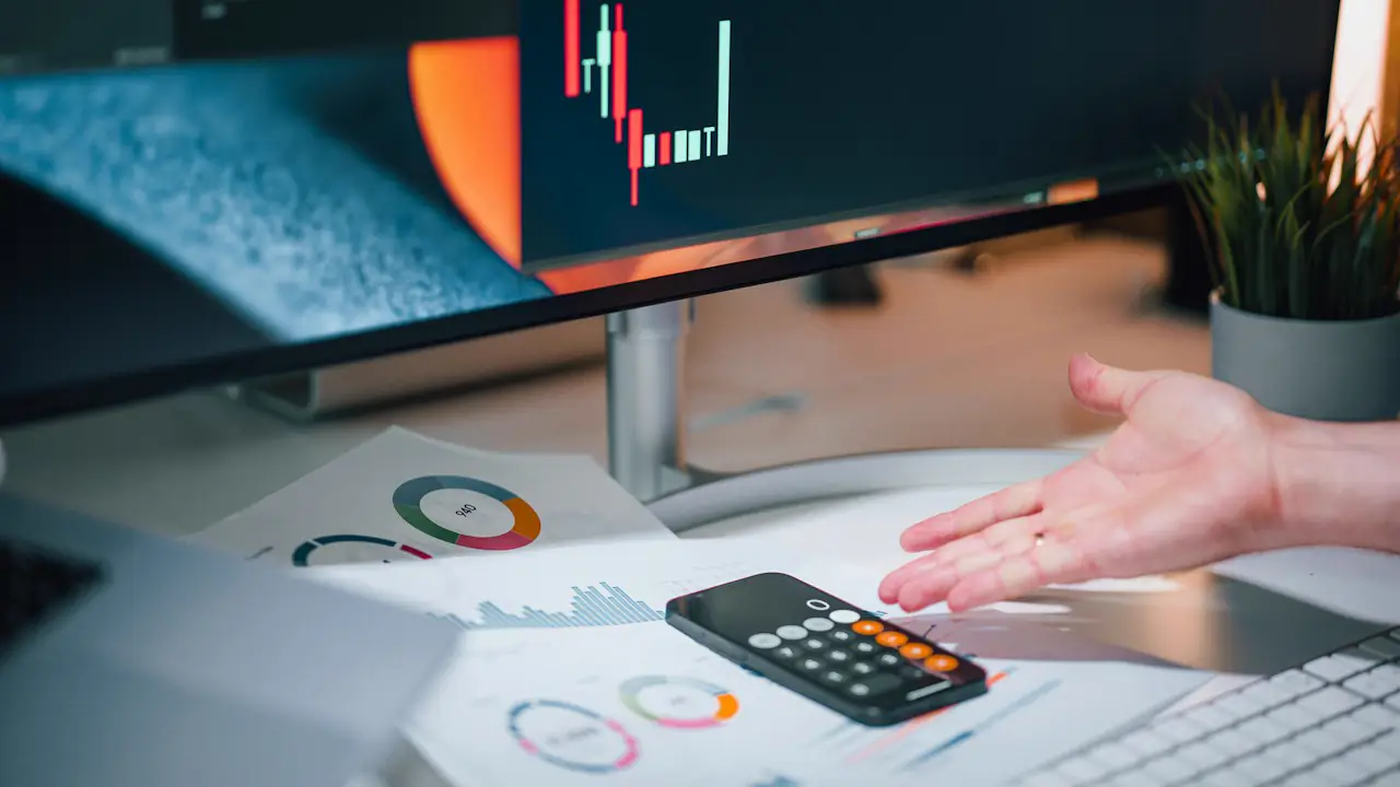 A desk with a calculator, printed charts and a monitor