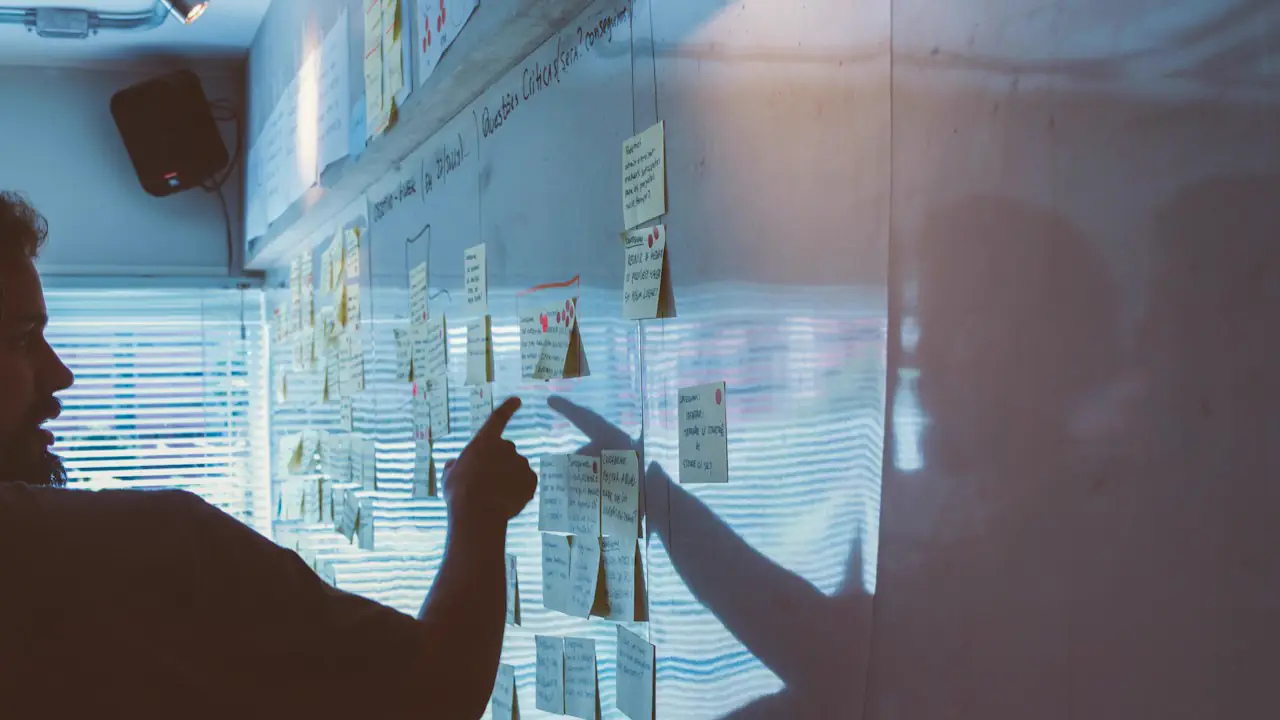 Two people pointing at sticky notes on a glass wall