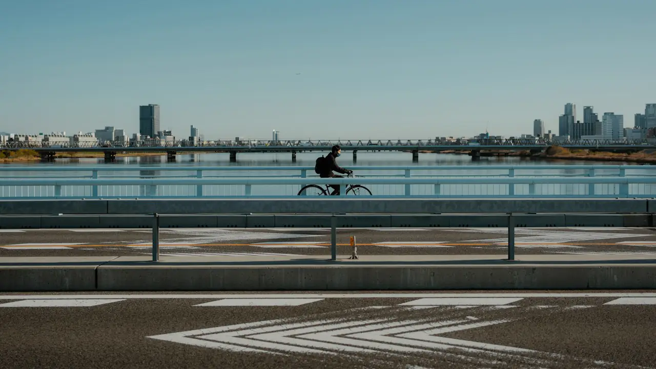 A cyclist crossing a long bridge with a city skyline in the distance