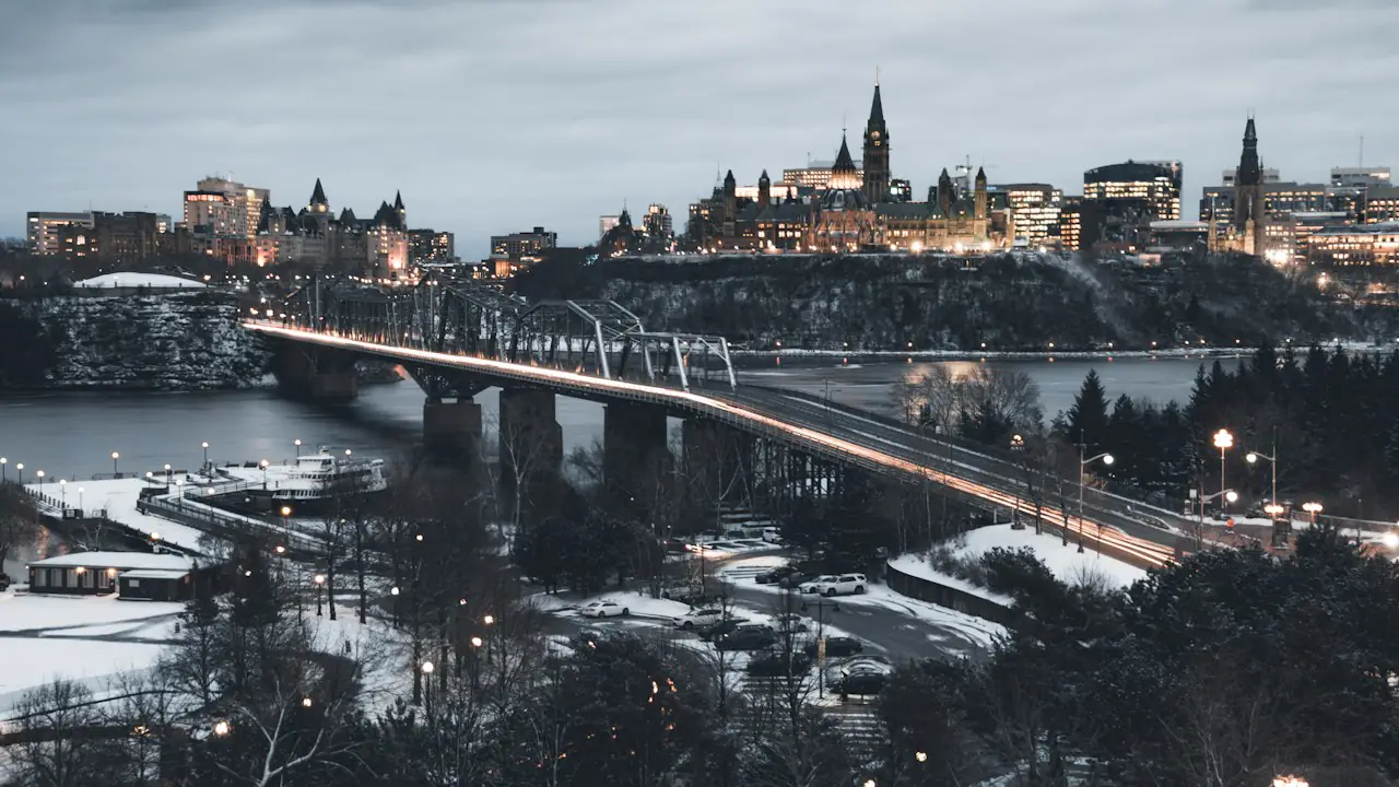 Parliament Hill and a lit bridge across the Ottawa River at dusk, seen from the Gatineau side