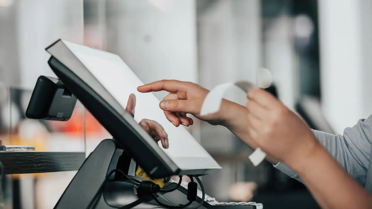 A shop assistant tapping a touchscreen till as a receipt prints