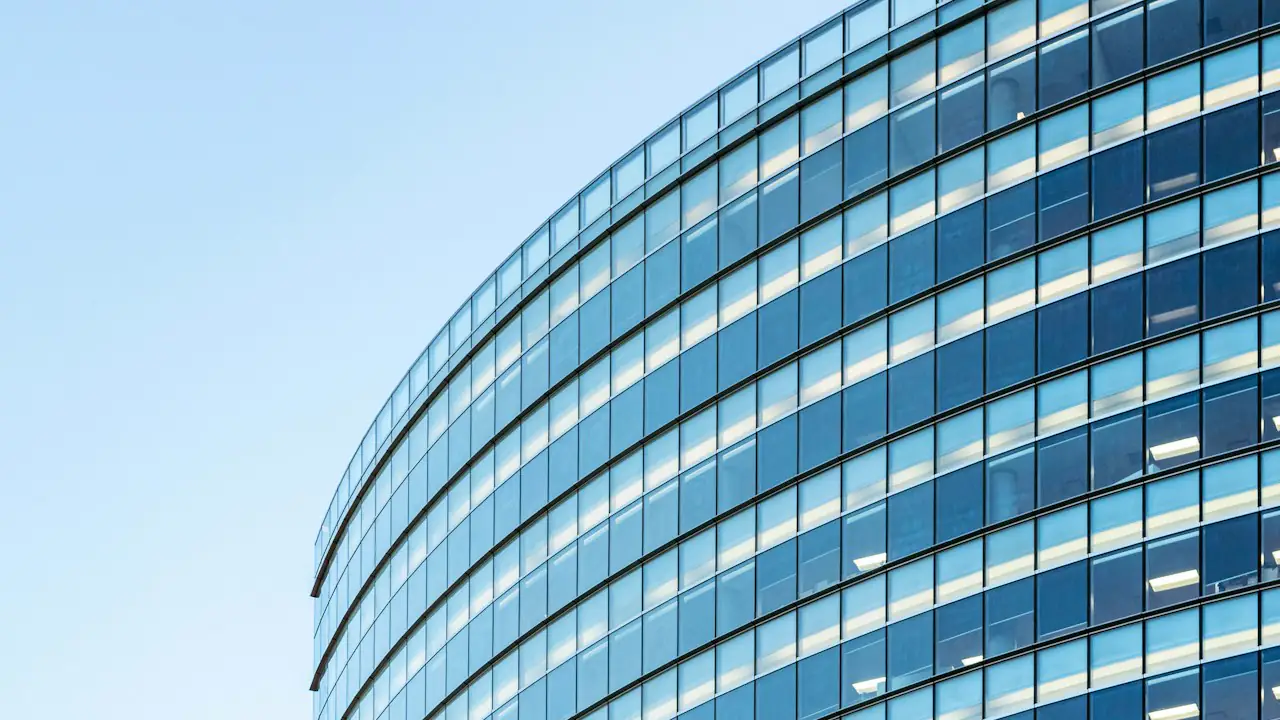 A curved glass office building against a blue sky
