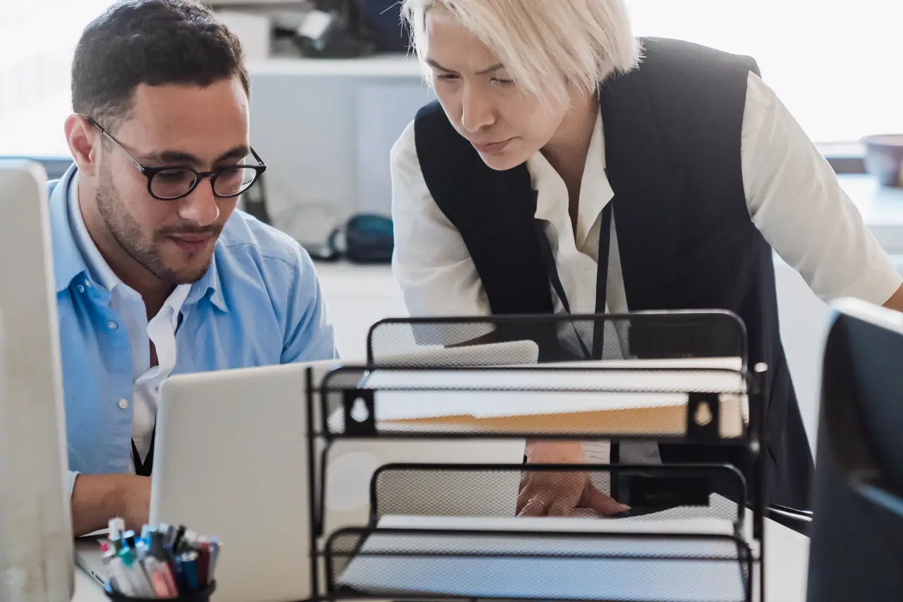 Two colleagues work together at a laptop in a bright modern office