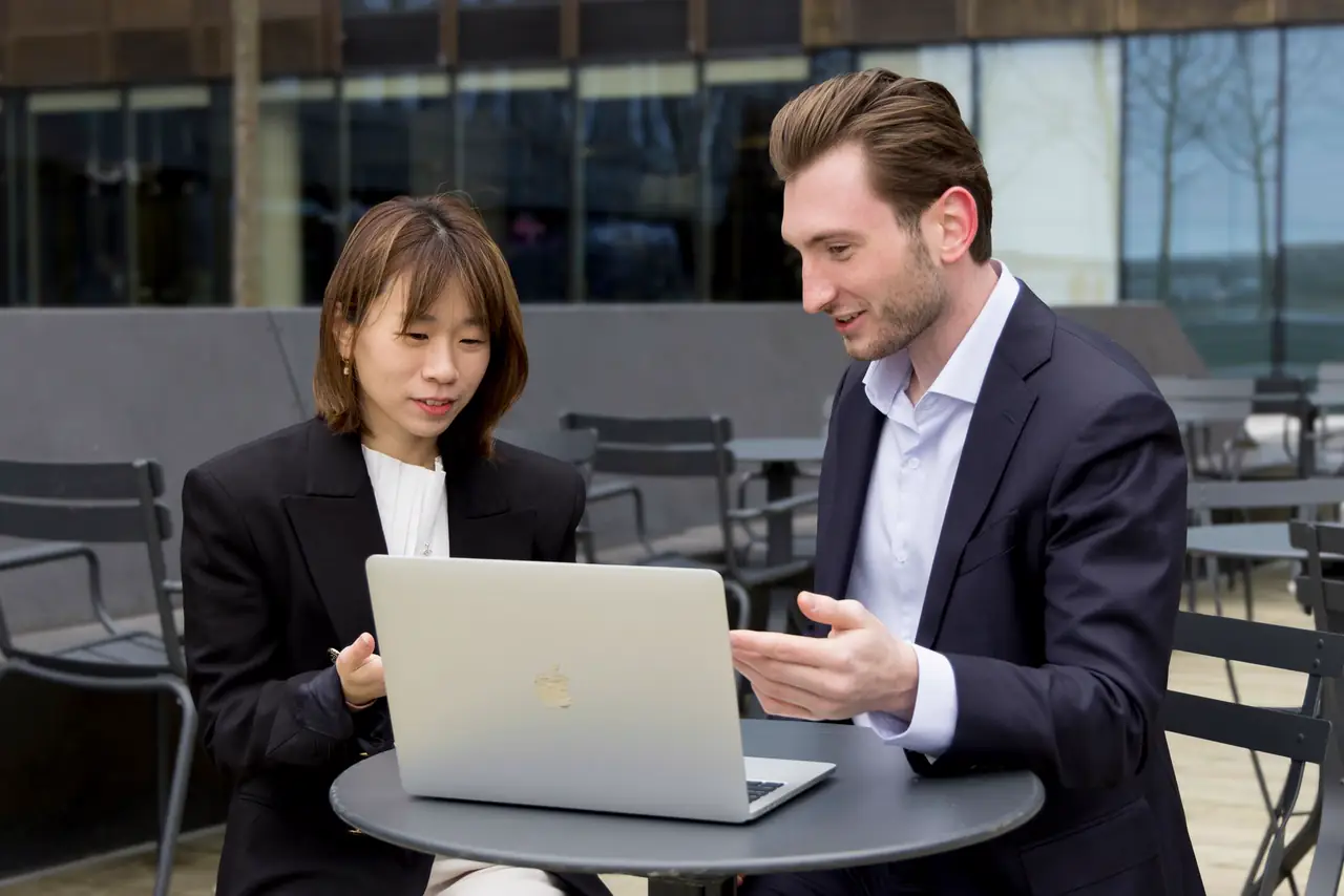 Two professionals go through work on a laptop during an outdoor meeting