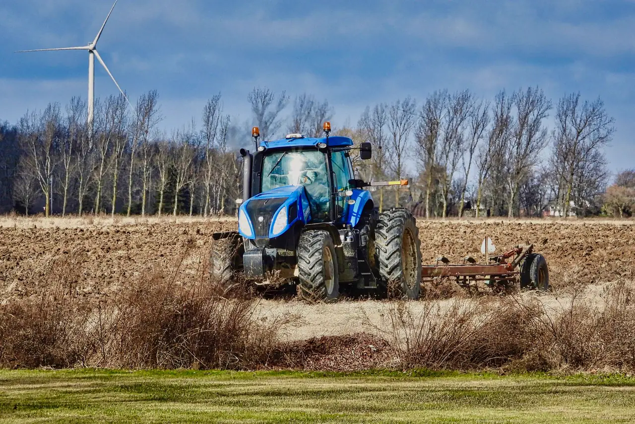 Blue tractor ploughs a field in Ontario, Canada with a wind turbine behind it
