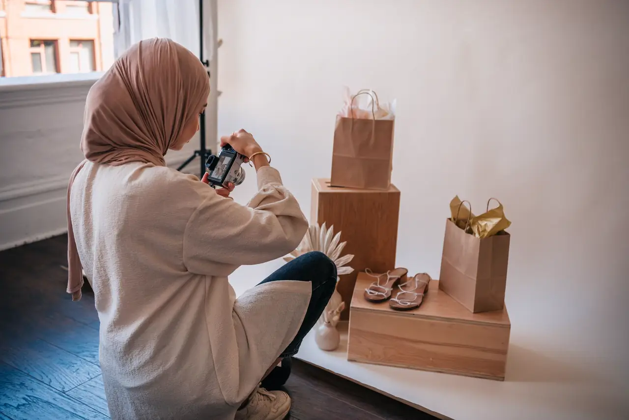 Seller in a hijab photographs paper bags and shoes on a product set at home
