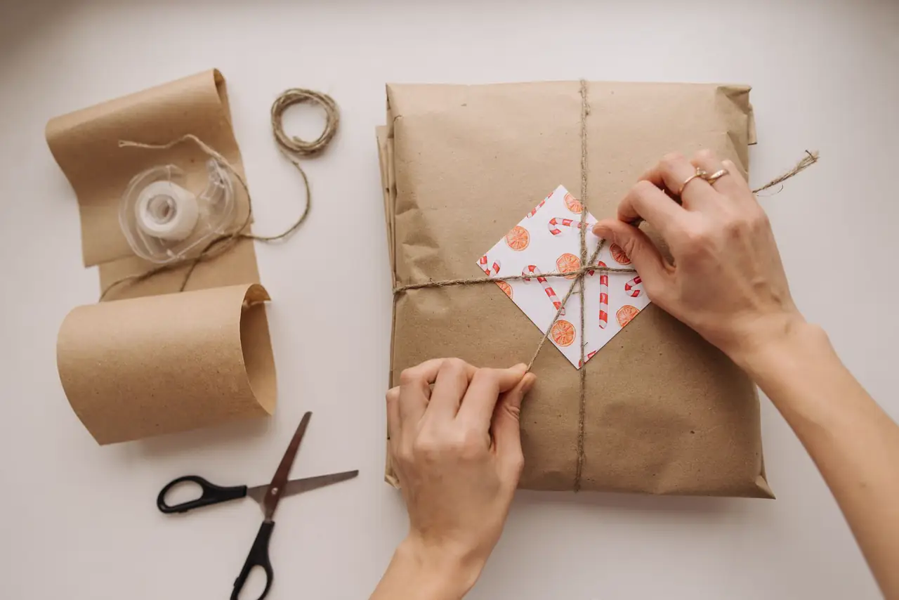 Hands tie a brown paper parcel with string on a work table