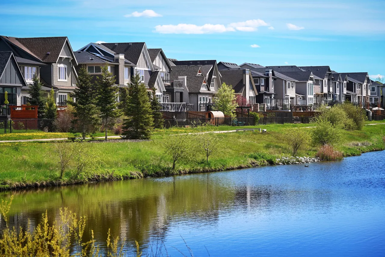 Row of modern suburban houses beside a calm pond with green grass in Airdrie, Alberta
