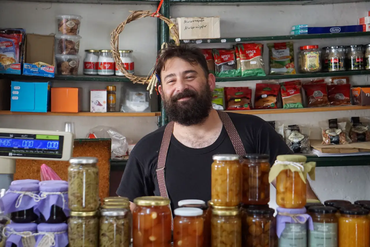 Friendly shopkeeper stands behind shelves filled with jars of homemade preserves