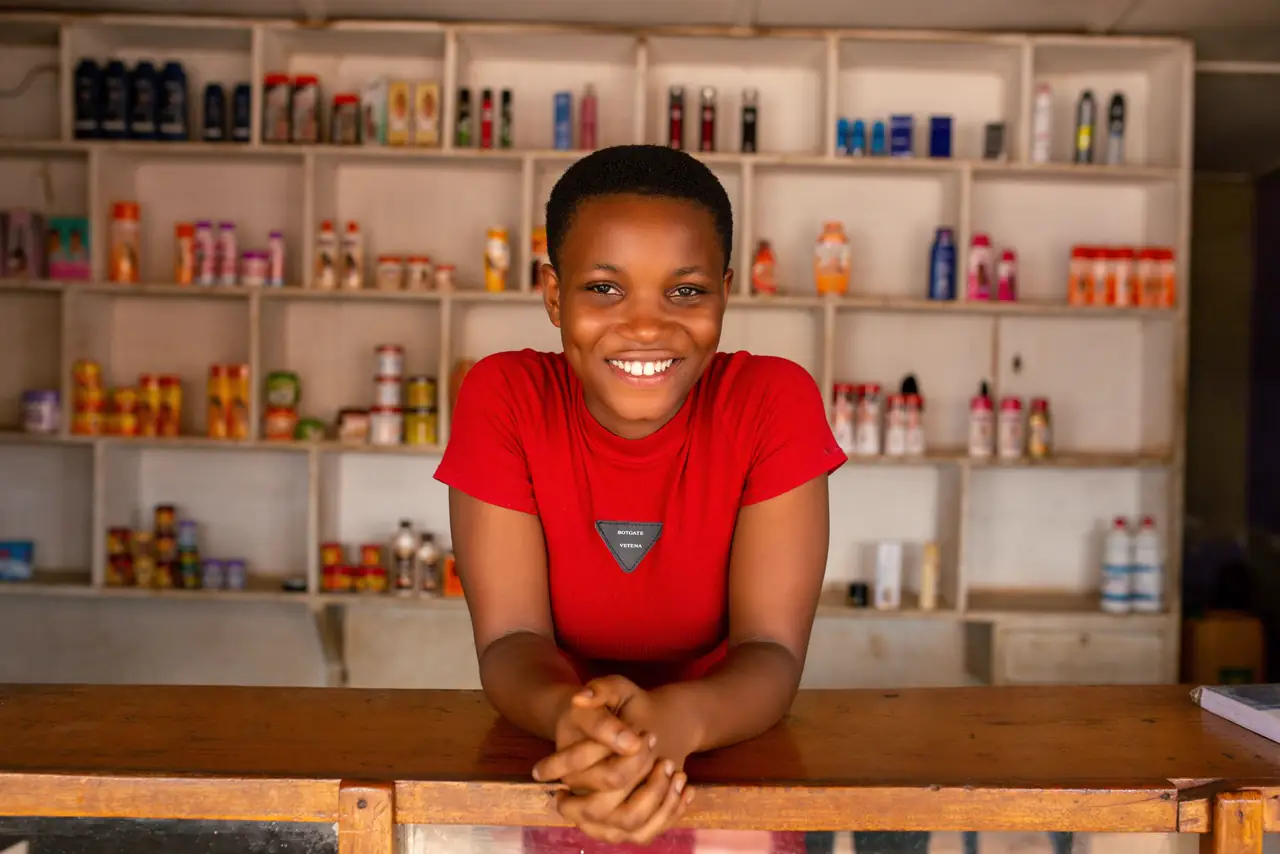 Cheerful shop owner smiles behind a wooden counter in front of well stocked shelves