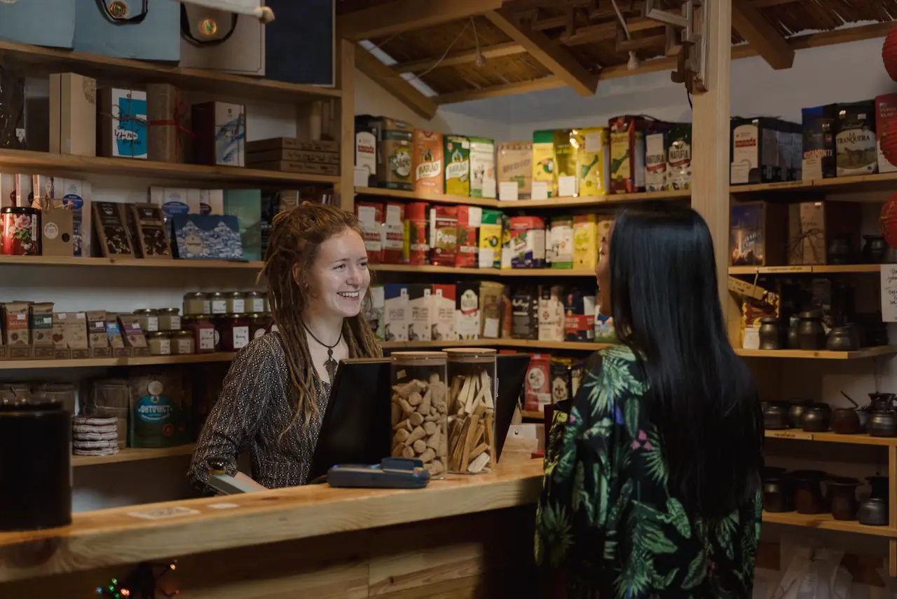 Shop owner helps a customer at the counter of a cosy well stocked store