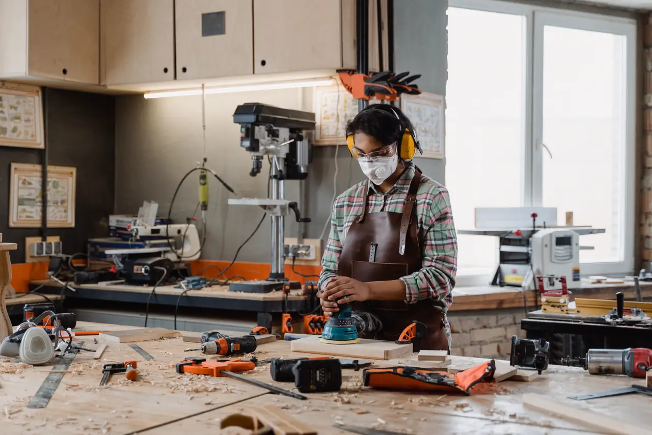 Woman carpenter sands a piece of wood in a well equipped workshop