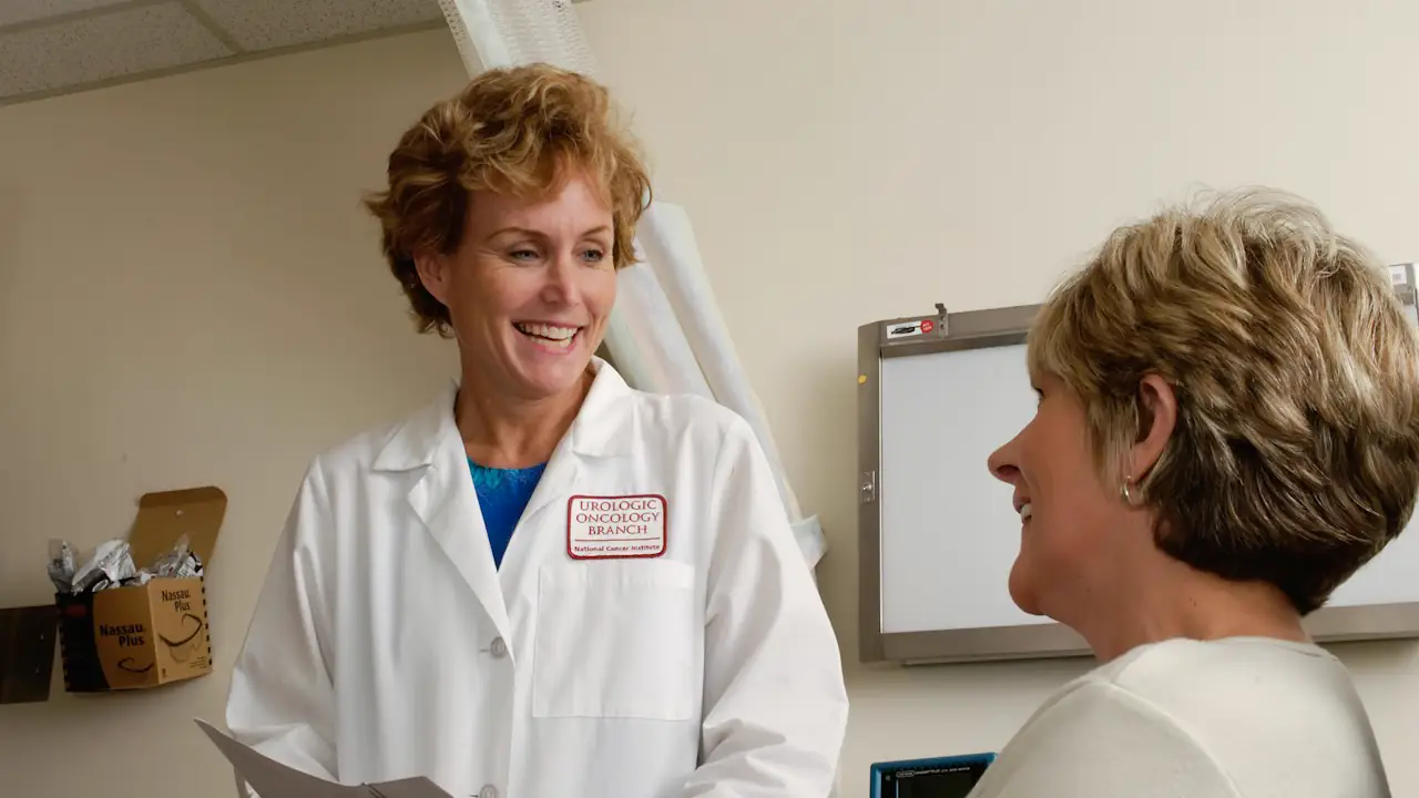 A smiling doctor in a white coat talking with a patient in a clinic office