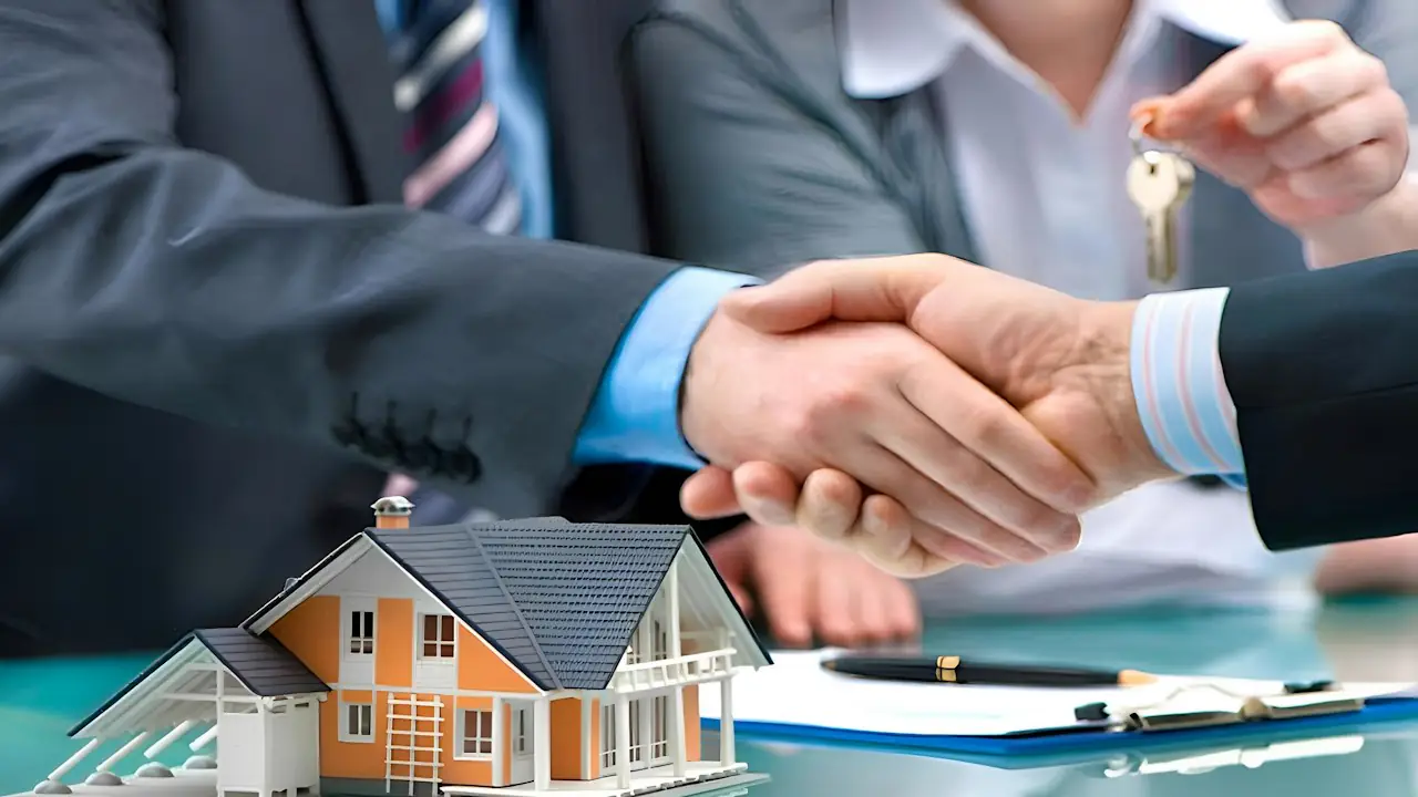 Two people shaking hands over a model house and a signed document