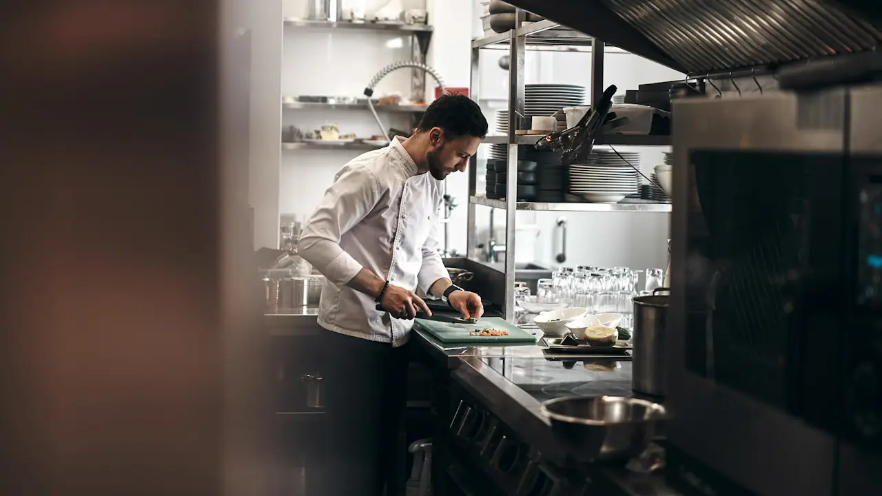 A chef preparing vegetables at a steel counter in a restaurant kitchen