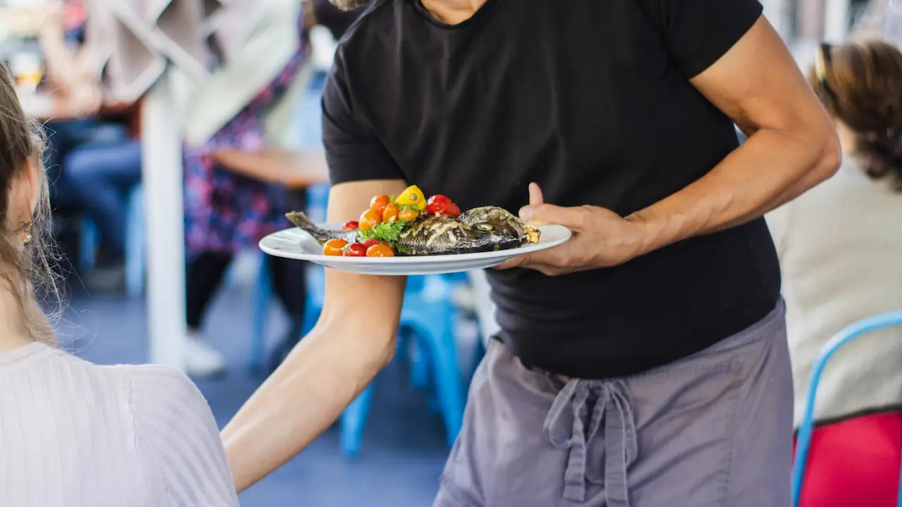 A server carrying a colourful plate of food to diners in a busy restaurant