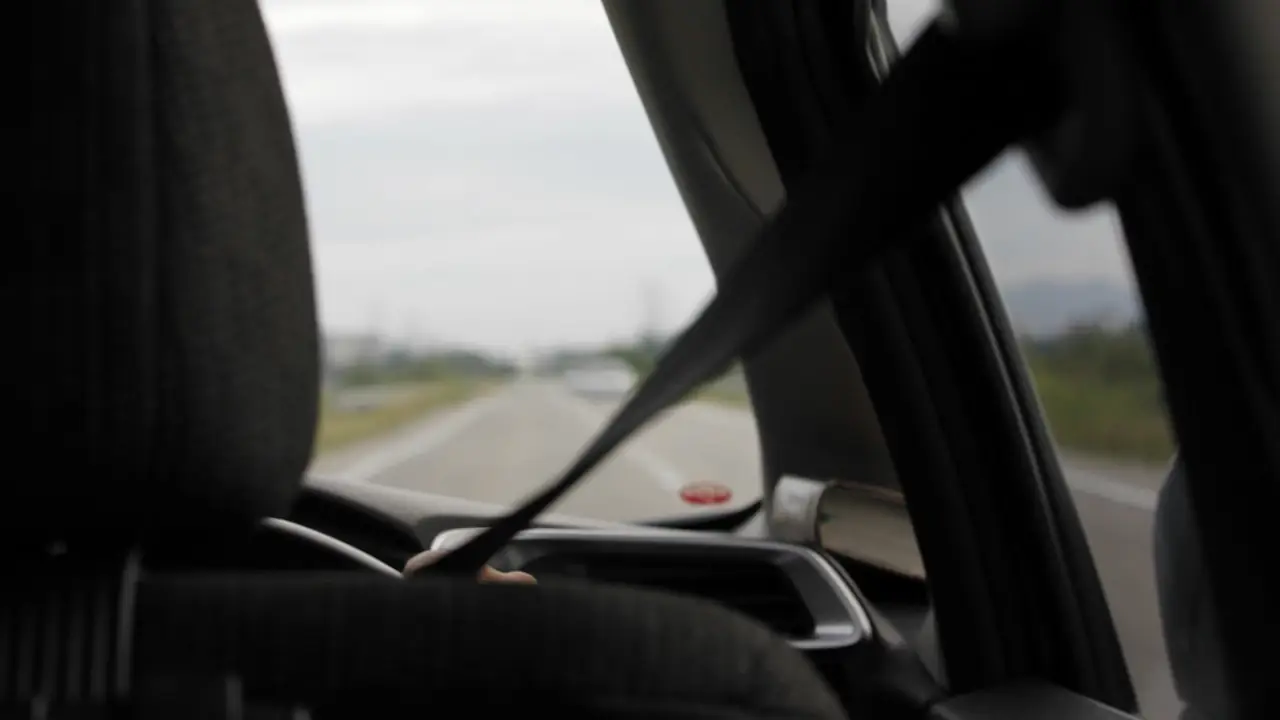 The view from a car's back seat, with a seat belt and an open highway ahead