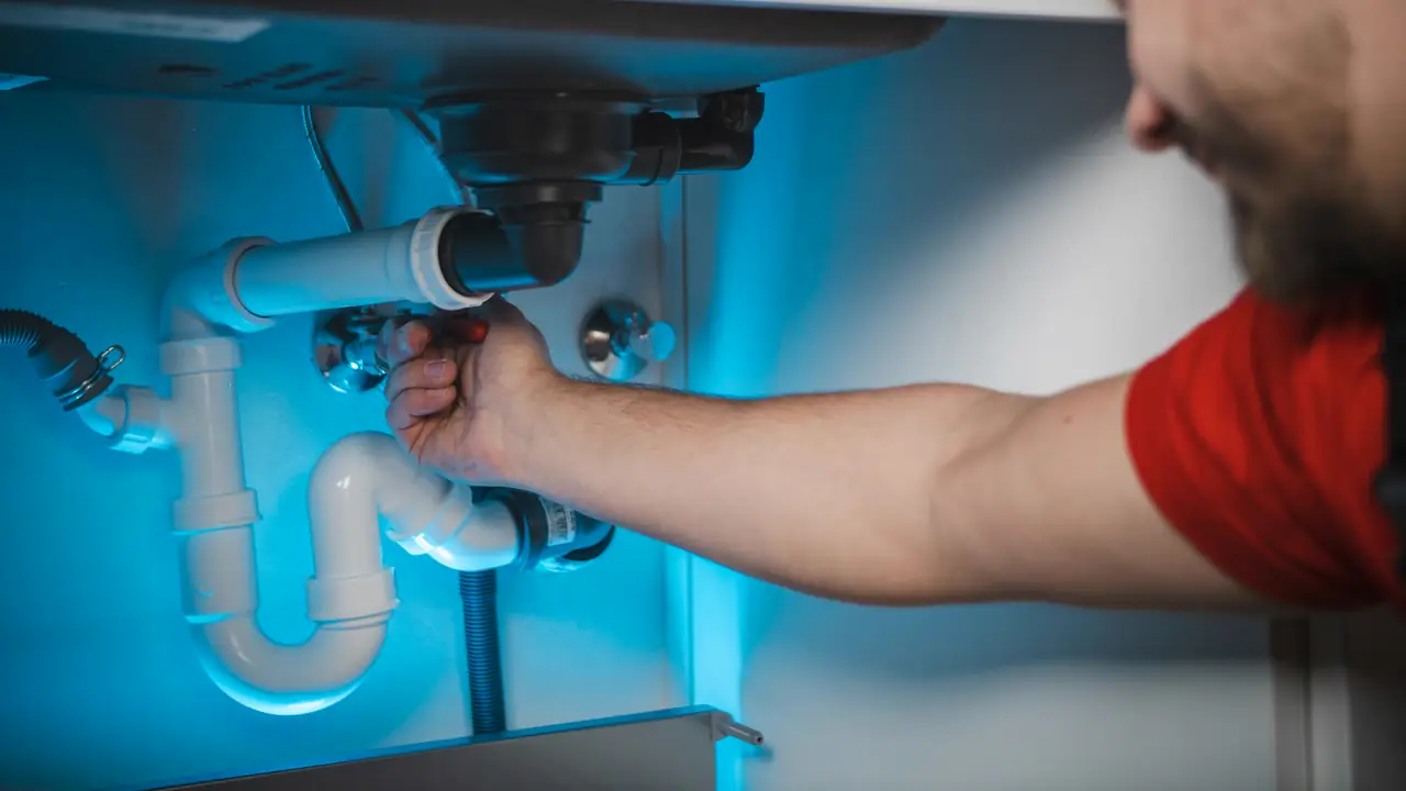 A plumber reaching under a sink to tighten a drain pipe