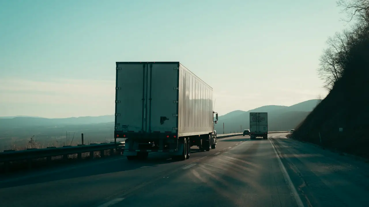 Two transport trucks travelling a highway through rolling hills at dusk