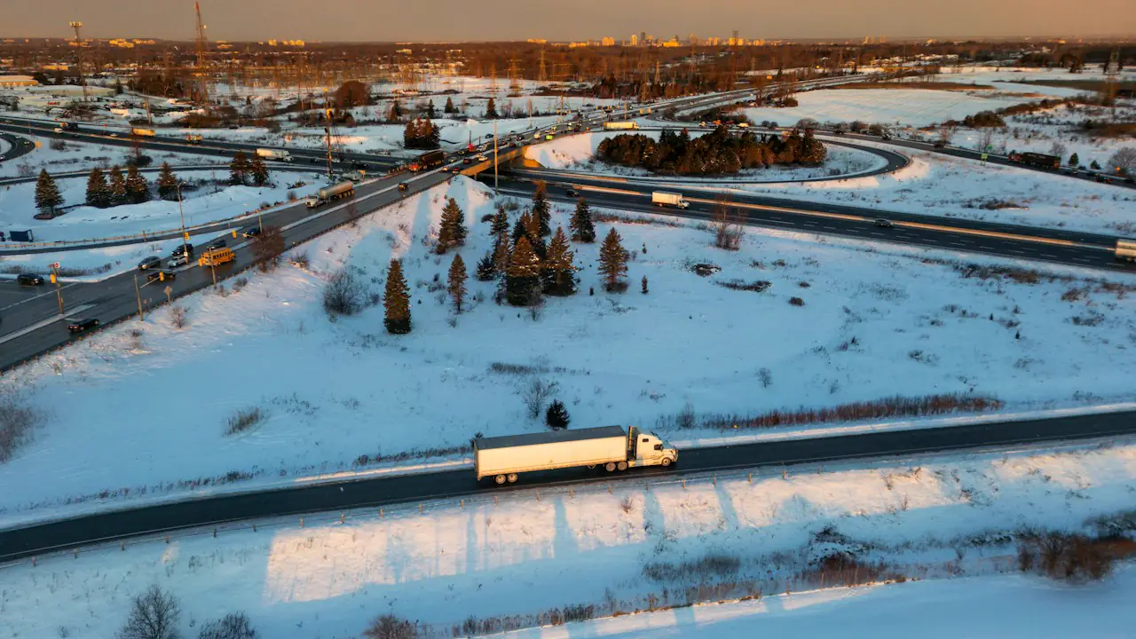 A transport truck on a snowy highway beside an interchange at sunset