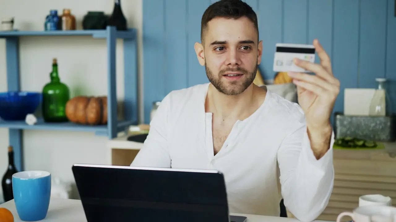 A man at a laptop holding up a bank card to make a payment