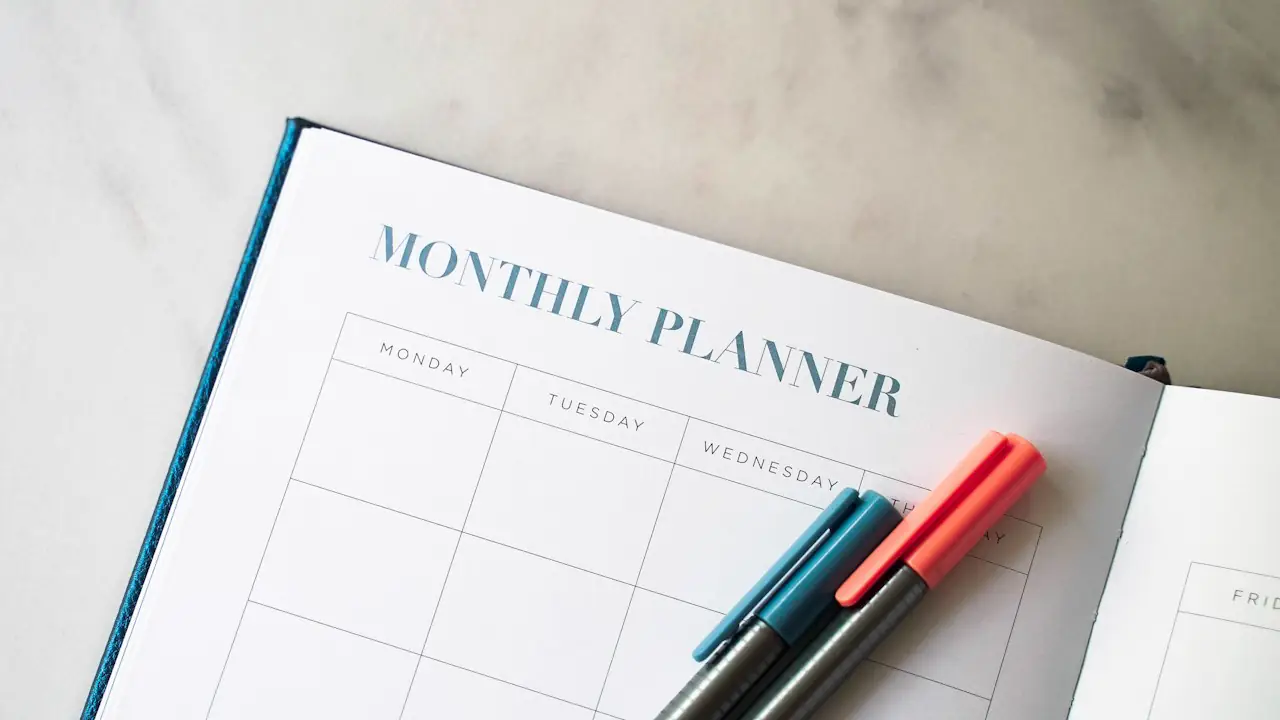 An open monthly planner with two pens resting on the page