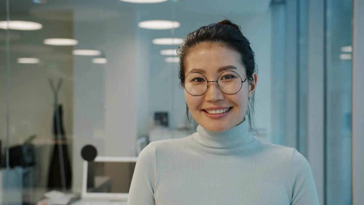 A smiling woman in glasses and a grey sweater standing in a bright office