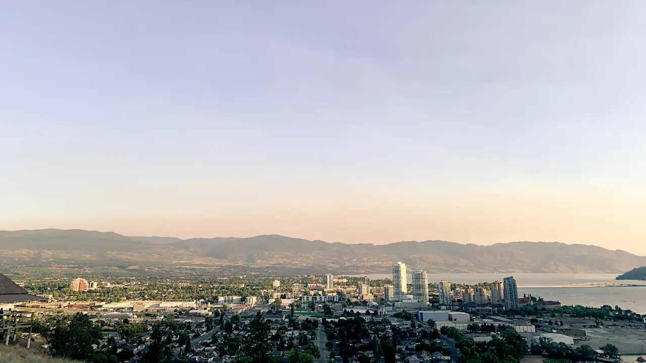 Downtown Kelowna and Okanagan Lake under a soft evening sky, with hills across the water