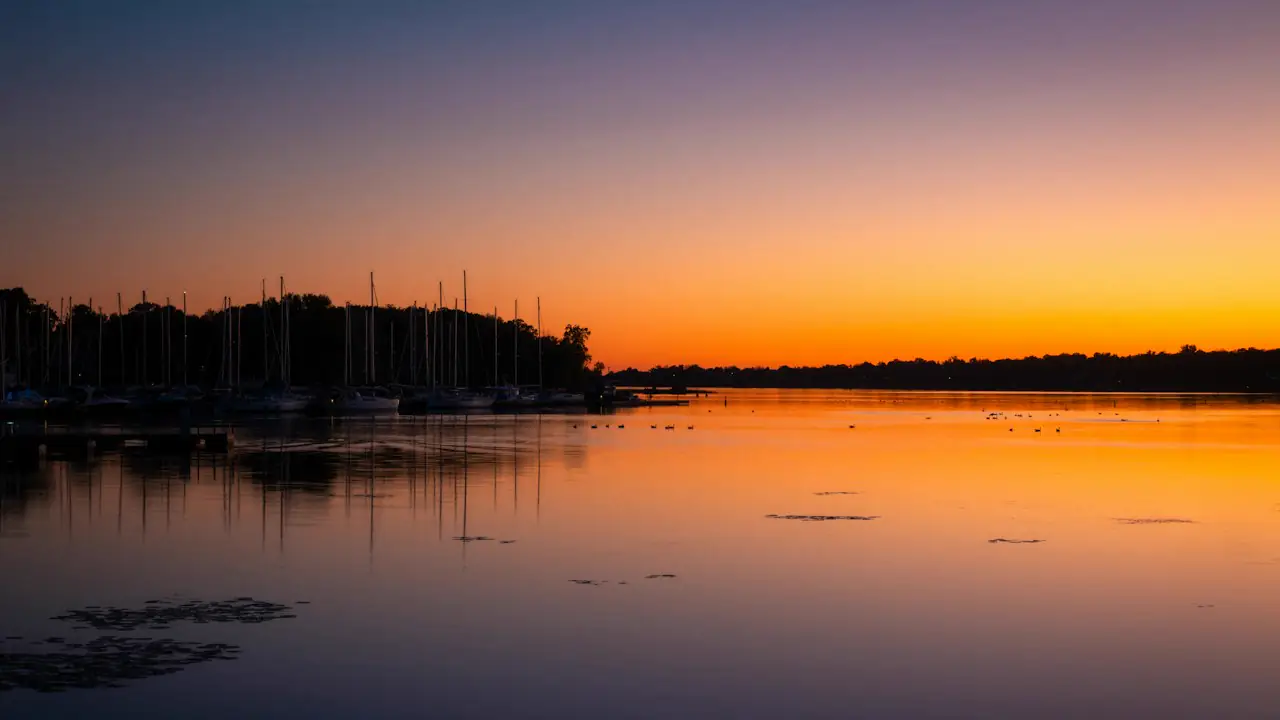 Sailboat masts silhouetted against an orange sunset over Collins Bay in Kingston