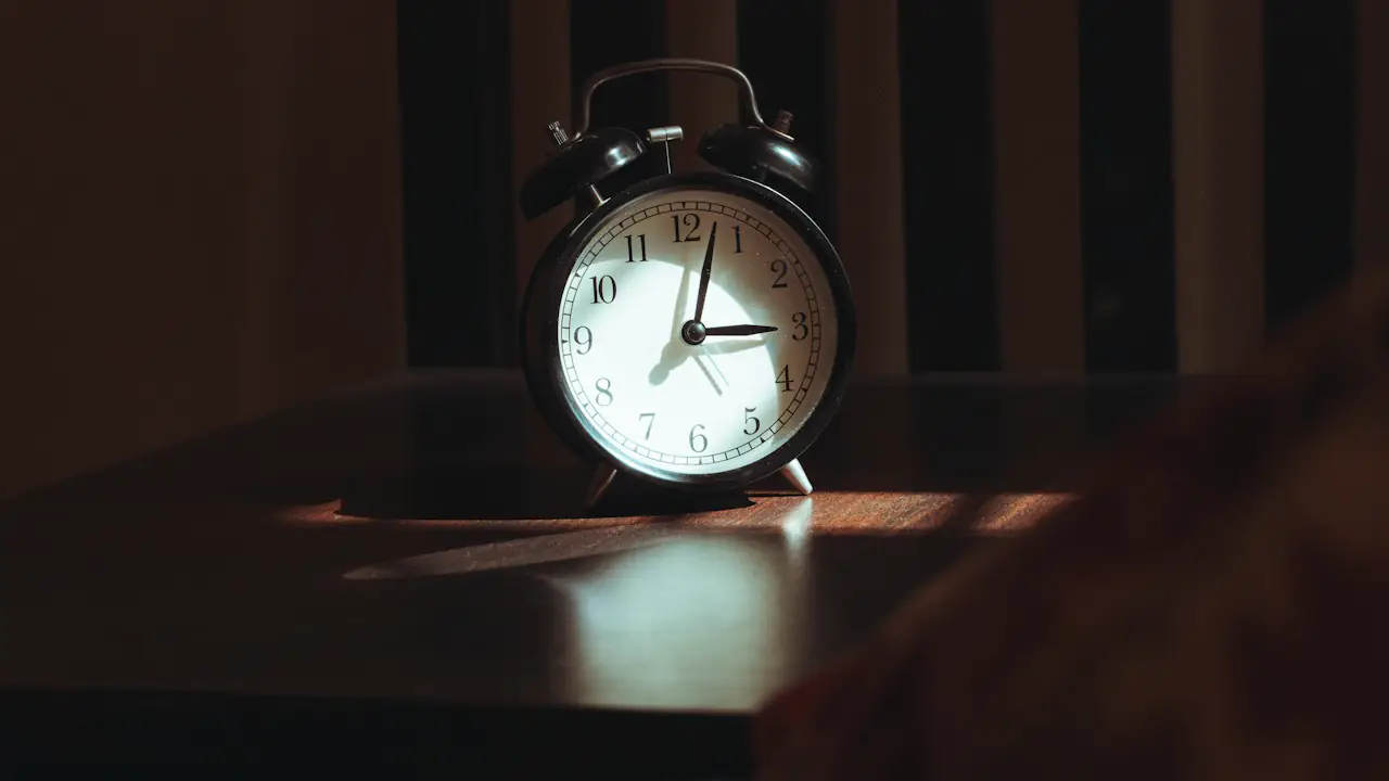 A classic alarm clock on a wooden table in low evening light